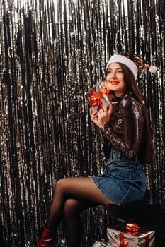 a girl in a shiny jacket with a Santa hat with gifts on a silver background in the form of rain.