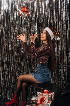 a girl in a shiny jacket with a Santa hat with gifts on a silver background in the form of rain.