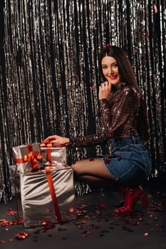 a girl in a shiny jacket and skirt with gifts on a silver background in the form of rain.