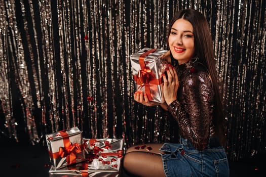 a girl in a shiny jacket and skirt with gifts on a silver background in the form of rain.