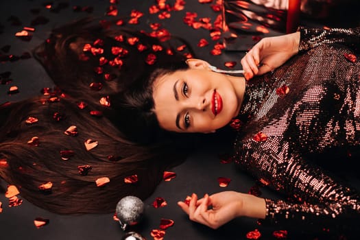 Top view of a girl lying in shiny clothes on the floor in confetti in the form of hearts.