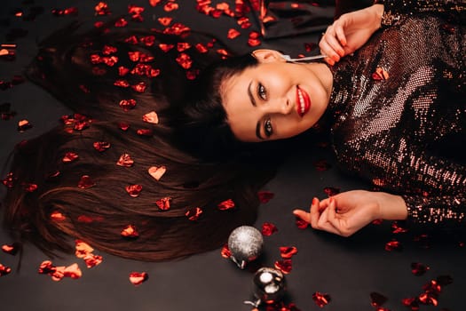 Top view of a girl lying in shiny clothes on the floor in confetti in the form of hearts.