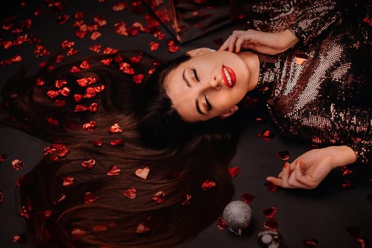 Top view of a girl lying in shiny clothes on the floor in confetti in the form of hearts.