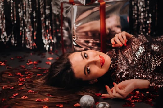 Top view of a girl lying in shiny clothes on the floor in confetti in the form of hearts and gifts.