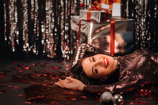 Top view of a girl lying in shiny clothes on the floor in confetti in the form of hearts and gifts.