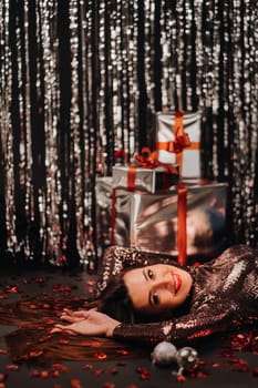 Top view of a girl lying in shiny clothes on the floor in confetti in the form of hearts and gifts.