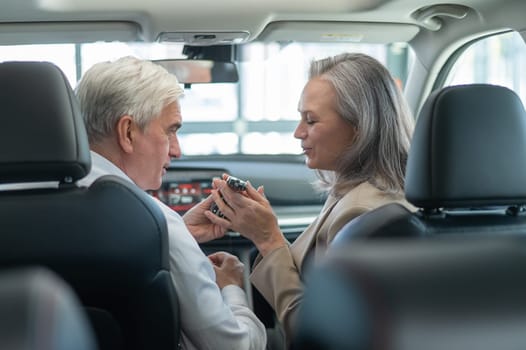 Mature Caucasian couple sitting in a new car and rejoicing at the purchase