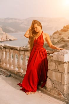 Woman red dress. Summer lifestyle of a happy woman posing near a fence with balusters over the sea