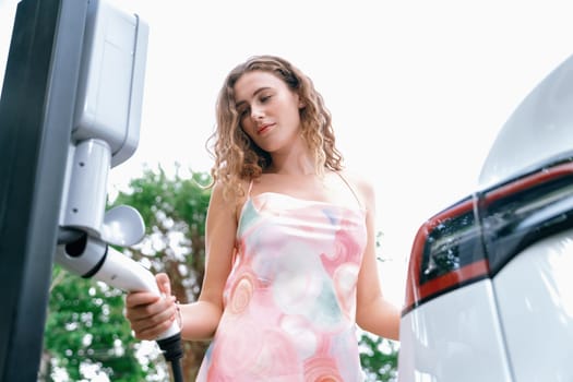 Eco-friendly conscious woman recharging modern electric vehicle from EV charging station. EV car technology utilized as alternative transportation for future sustainability. Synchronos