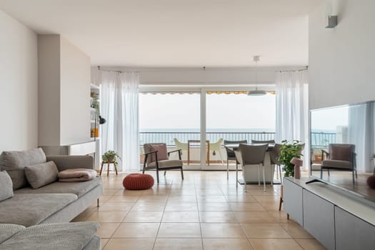 Light spacious living room with large balcony at seaside. Luxury home apartment with elegant grey furniture and panoramic window. Interior design