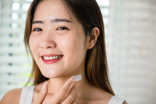 Asian beautiful young woman applying cosmetic cream on neck at home, Happy female apply lotion moisturizer on her neck after shower, Beauty skin care cosmetic protect and nourish skin concept