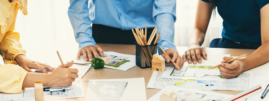 A portrait of professional architect team discussion about architectural project on meeting table with blueprint and wooden block scatter around at modern office. Closeup. Focus hand. Delineation.