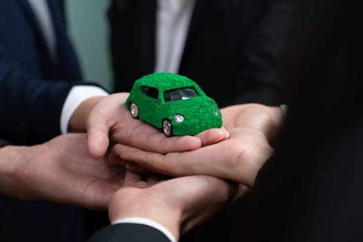 Business people holding EV car model as business synergy partnership unite and take action to utilized eco-transportation to reduce CO2 emission for sustainable and greener future. Quaint