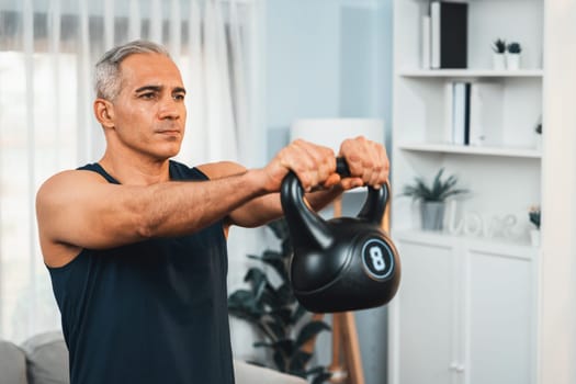 Athletic and sporty senior man engaging in body workout routine with lifting kettlebell at home as concept of healthy fit body with body weight lifestyle after retirement. Clout