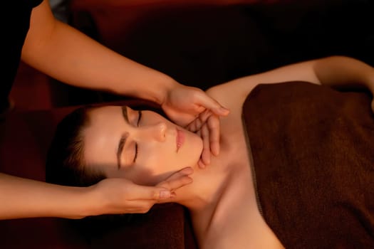 Caucasian woman enjoying relaxing anti-stress head massage and pampering facial beauty skin recreation leisure in warm candle lighting ambient salon spa in luxury resort or hotel. Quiescent