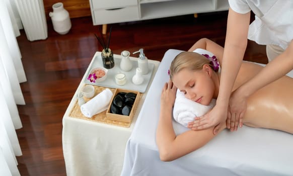 Caucasian woman customer enjoying relaxing anti-stress spa massage and pampering with beauty skin recreation leisure in day light ambient salon spa at luxury resort or hotel. Quiescent