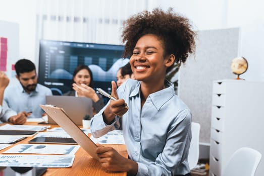 Portrait of happy young african businesswoman with group of office worker on meeting with screen display business dashboard in background. Confident office lady at team meeting. Concord