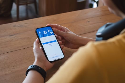 CHIANG MAI ,THAILAND - NOV 16, 2023 : Woman hand holding iPhone 14 to use facebook with new login screen.Facebook is a largest social network and most popular social networking site in the world..