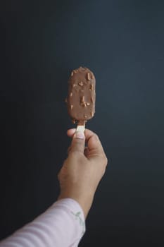 Hand holding melting ice cream on dark background.