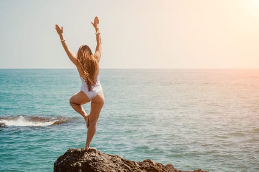 Woman sea yoga. Back view of free calm happy satisfied woman with long hair standing on top rock with yoga position against of sky by the sea. Healthy lifestyle outdoors in nature, fitness concept