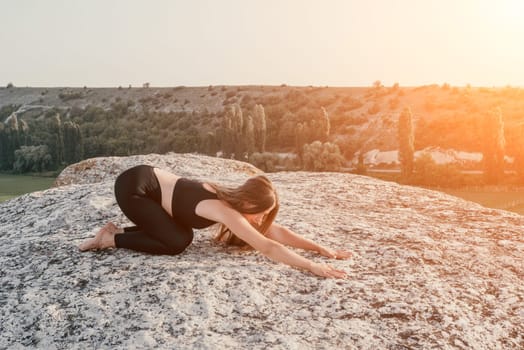 Well looking middle aged woman with long hair, fitness instructor in leggings and tops doing stretching and pilates on the rock near forest. Female fitness yoga routine concept. Healthy lifestyle.