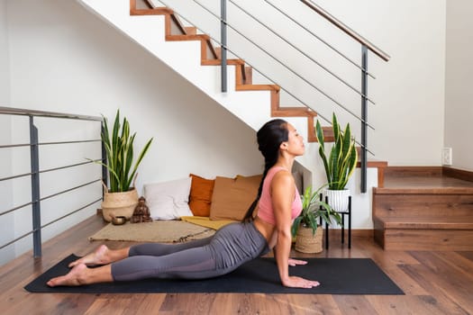 Young asian woman doing upward facing dog yoga pose at home living room. Wellness and healthy lifestyle concept.