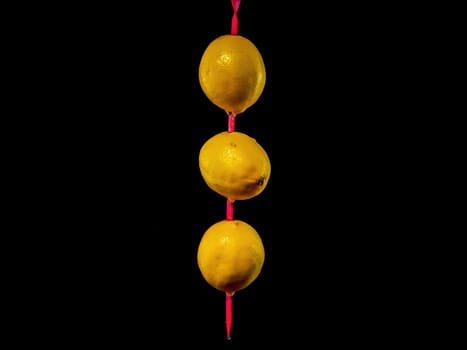 Creative still life with three lemons on a skewer on a black background