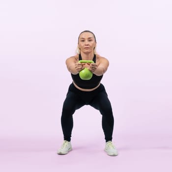 Full body length shot athletic and sporty senior woman doing squat with kettlebell for body workout on isolated background. Healthy active physique and body care lifestyle after retirement. Clout