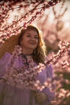 Woman blooming peach orchard. Against the backdrop of a picturesque peach orchard, a woman in a long pink dress and hat enjoys a peaceful walk in the park, surrounded by the beauty of nature