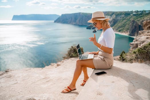 Freelance women sea working on the computer. Good looking middle aged woman typing on a laptop keyboard outdoors with a beautiful sea view. The concept of remote work