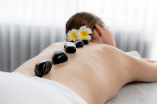 Hot stone massage at spa salon in luxury resort with day light serenity ambient, blissful woman customer enjoying spa basalt stone massage glide over body with soothing warmth. Quiescent