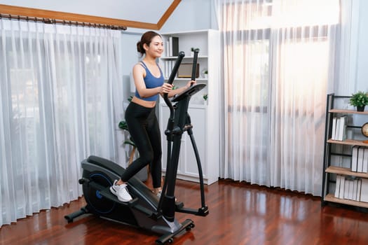 Energetic and strong athletic asian woman running on elliptical running machine at home. Pursuit of fit physique and commitment to healthy lifestyle with home workout and training. Vigorous