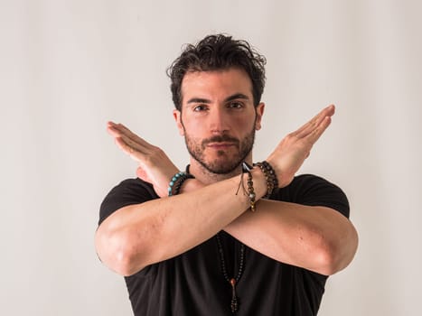 A man wearing a black shirt and bracelets, making an X sign with his arms, looking at camera