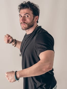 A Fashionable Man in a Black Shirt and Bracelets Ready to Throw a Punch Towards the Camera, on white background