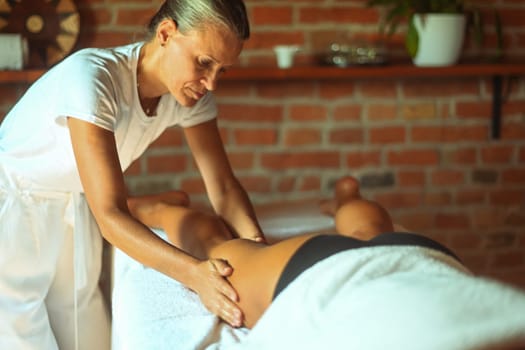 professional caucasian female physiotherapist masseuse performing leg massage to hispanic latino brunette woman in spa clinic
