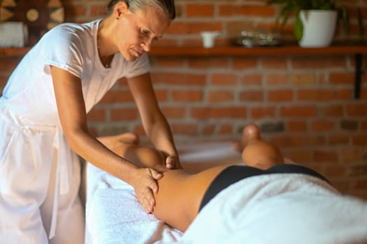 professional caucasian female physiotherapist masseuse performing leg massage to hispanic latino brunette woman in spa clinic