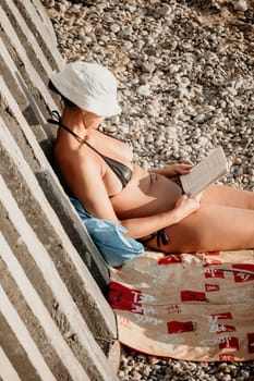 Beautiful Young Woman reading book and Sitting on the Beach Chair Under Beach Umbrella on Vacation. Summer Holidays Travel Concept.