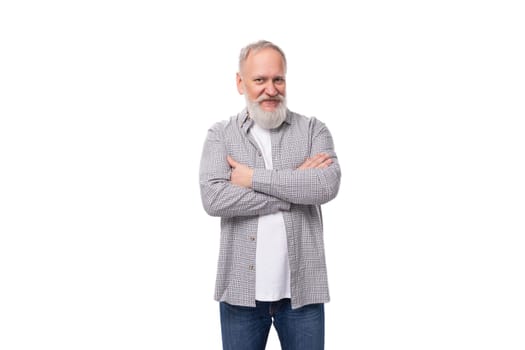 well-groomed senior man with a gray beard and mustache is dressed in a plaid shirt and jeans on a white background with copy space.