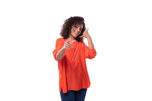 young stylish curly Caucasian brunette woman dressed in an orange blouse points with her index finger. advertising concept.