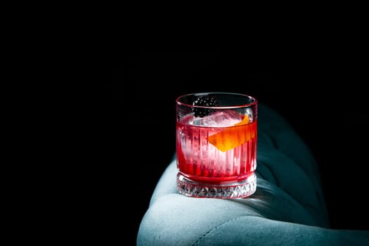 red cocktail in a transparent glass with round ice, whipped cream and black berry on top