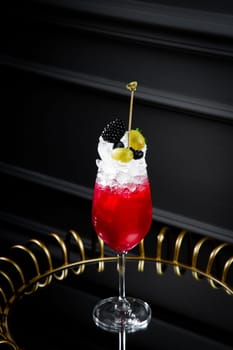 red cocktail in a transparent glass with round ice, whipped cream and black berry on top