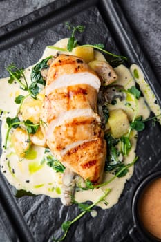 side view of chicken breast in cheese sauce with herbs on a black tray. High quality photo