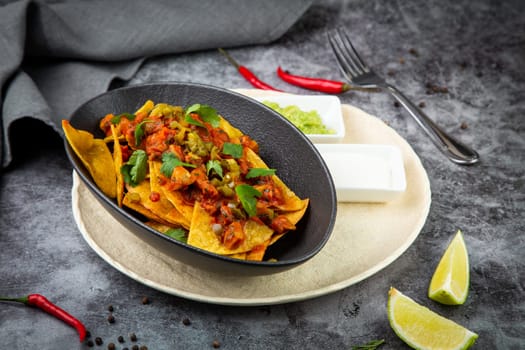 nachos with sauce, meat and herbs in a black plate