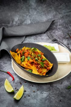 nachos with sauce, meat and herbs in a black plate