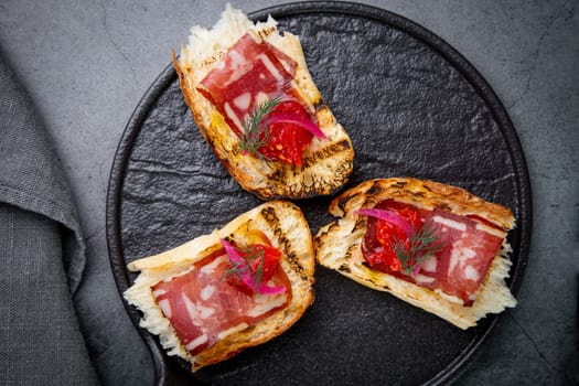 Fried bruschetta with dried venison on a black plate