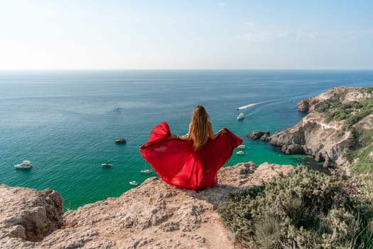 Woman sea red dress yachts. A beautiful woman in a red dress poses on a cliff overlooking the sea on a sunny day. Boats and yachts dot the background