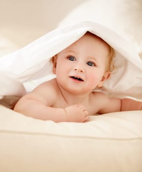 Happy, face and baby on a bed with blanket for playing, games or fun in a nursery room. Learning, child development and curious boy kid in a bedroom with sheet cover while lying, resting or relax.