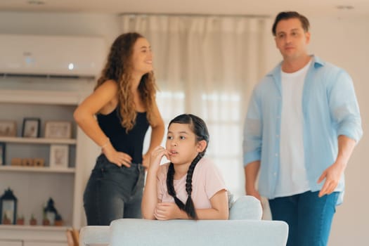 Annoyed and unhappy young girl sitting on sofa trapped in middle of tension by her parent argument in living room. Unhealthy domestic lifestyle and traumatic childhood develop to depression.Synchronos