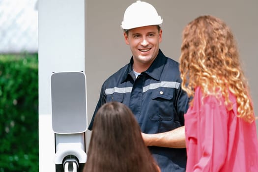 Technician install home EV charging station, providing service support for EV app on customer smartphone for monitoring charging status and set charging schedules at home. Synchronos