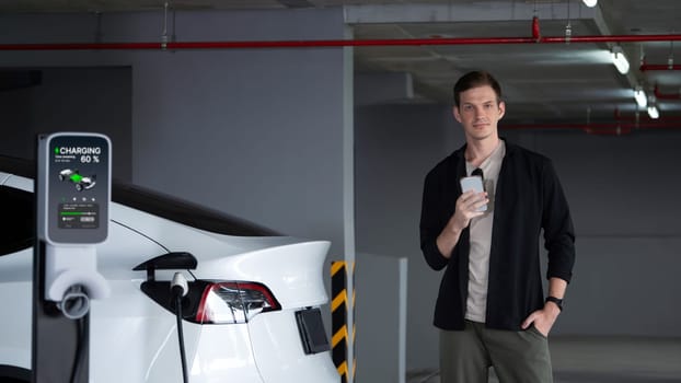 Young man travel with EV electric car to shopping center parking lot charging in downtown city showing urban sustainability lifestyle by green clean rechargeable energy of electric vehicle innards